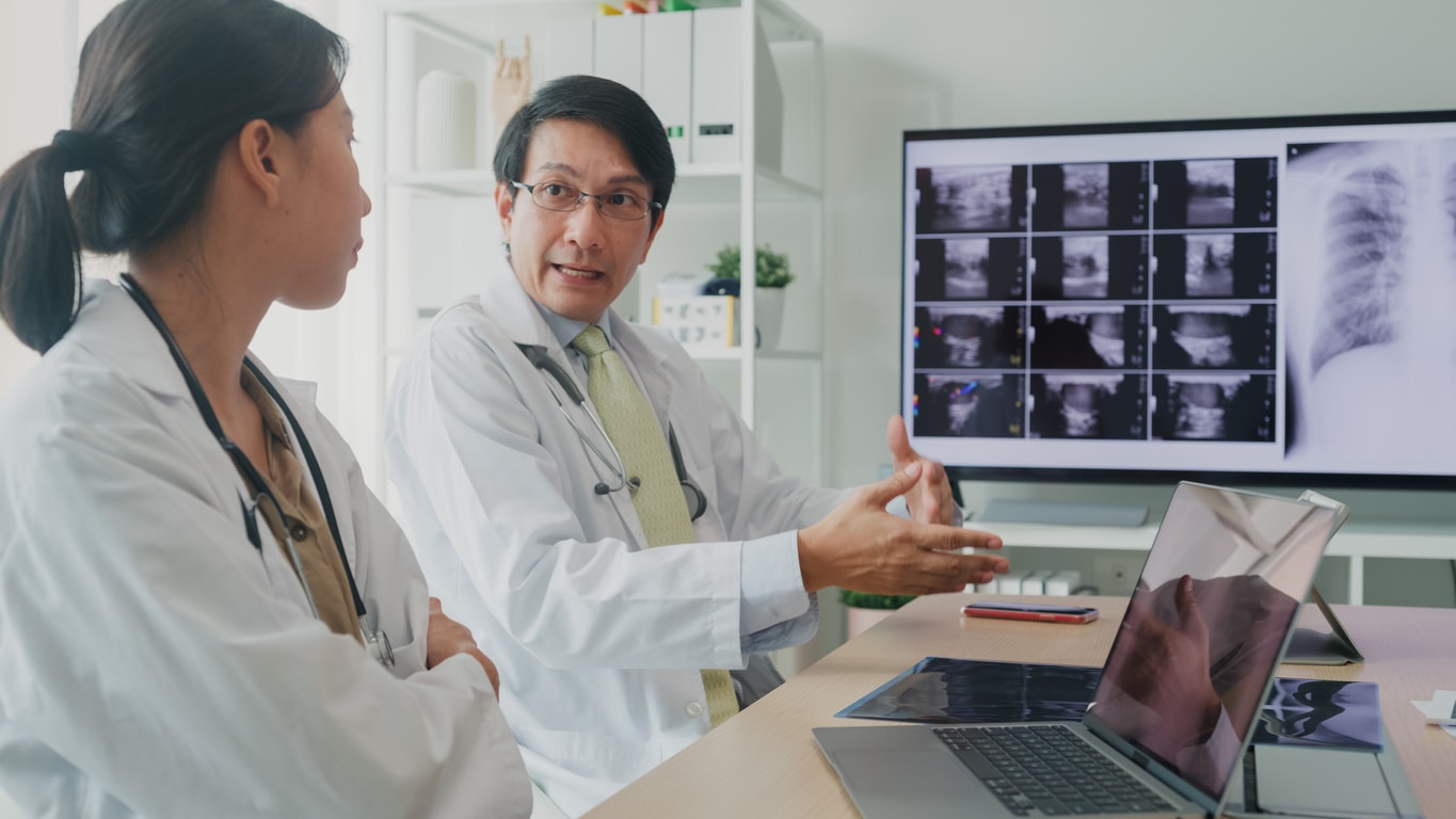 Two Asian doctors discussing a series of x-ray images on a computer